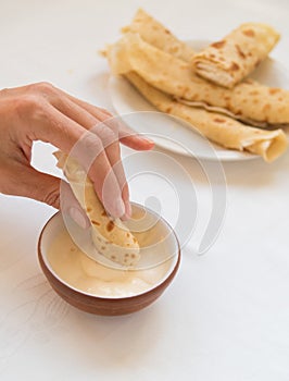 Female hand dipping pancake roll into sour cream.