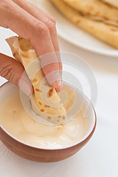 Female hand dipping pancake roll into sour cream.