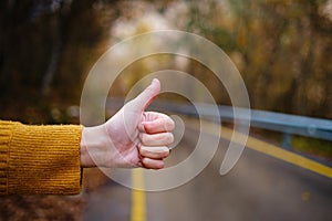 female hand doing hitchhiking sign near the country roadside.