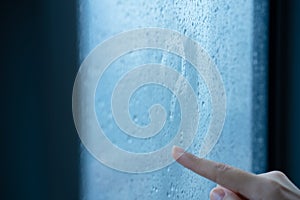 Female hand draws a question mark on a foggy window during the rain. A glass in drops of water