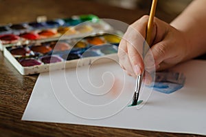 Female hand draws with watercolors on a white sheet of paper