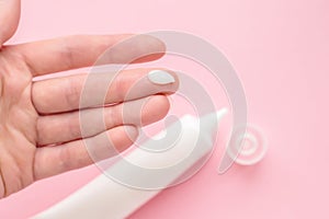 Female hand with a drop of cream on a finger. Jar  bottle  tube of cream isolated on a pink background