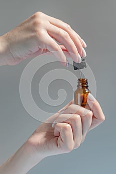 female hand with Dropper of essential oil, aromatherapy essence, beauty serum or medicinal liquid on beige background