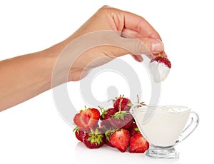 Female hand dunked strawberry into cup with cream
