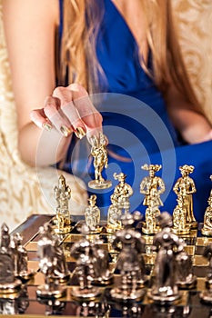 Female hand with elegant gold manicure holding chess piece