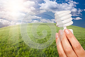 Female Hand with Energy Saving Light Bulb Over Fie