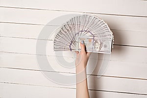 Female hand with a fan of 100 dollar American banknotes on a white wooden table background