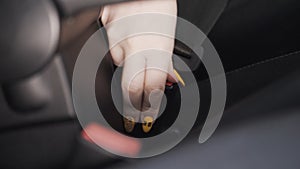 Female hand fastens a seat belt inside a car. Action. Close up of female hand with bright yellow manicure fastening seat