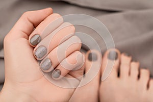 Female hand and feet with brown nail design. Beige nail polish manicure and pedicure on brown fabric