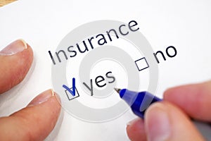 female hand fills out a questionnaire with check-box - insured yes or no? insurance checklist selection over a white background