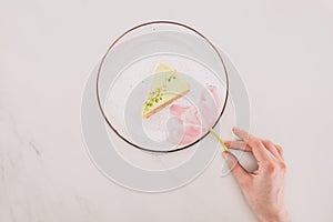 Female hand, flower and piece of cake on plate on white tabletop