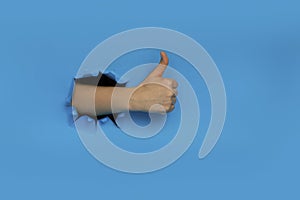 Female hand gestures ok approval sign keeps thumb up recommends something breaks through blue paper background. Copy