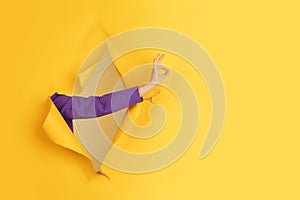 Female hand gesturing in torn yellow paper hole background