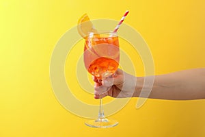 Female hand with glass aperol spritz cocktail on yellow background