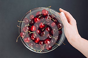 Female hand and glass bowl with juicy and red cherries