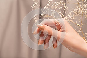 Female hand with glitter beige nail design. Female hand hold dry autumn flower. Woman hand on beige fabric background