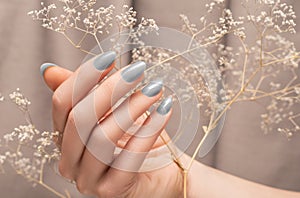 Female hand with glitter silver nail design. Female hands hold autumn flower. Woman hand on beige fabric background