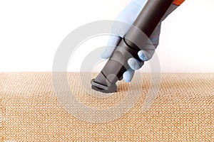 A female hand in a glove vacuums the surface of the sofa.