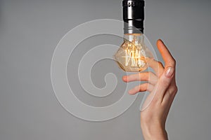 Female hand with glowing light bulb on grey background