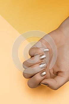 Female hand with gold nail design. Golden nail polish manicured hand. Female hand on orange beige background