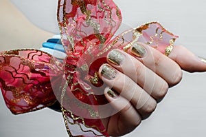 Female hand with gold nail design and red bow.