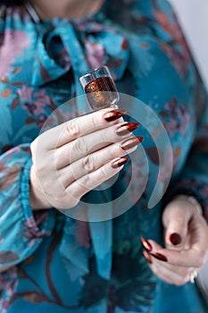 Female hand with golden brown maroon, manicure holds a bottle of nail polish