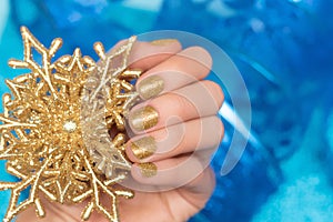 Female hand with golden nail design. Glitter gold nail polish manicure. Model hand hold gold Christmas star decoration on blue