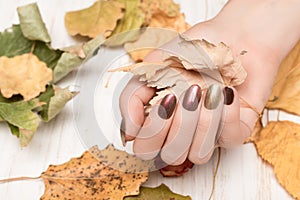 Female hand golden with nail design. Gold and red nail polish manicure. Woman hand hold yellow autumn leaf