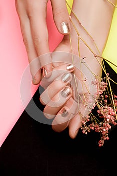 Female hand with golden nail design. Golden nail polish manicure. Female hand on pink black yellow background