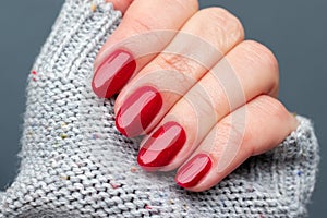 Female hand in a gray knitted sweater fabric with beautiful manicure - red glittered nails