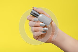 Female hand with gray nail design. Gray nail polish manicure. Woman hold gray varnish on yellow background