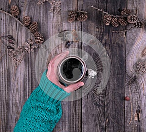 female hand in a green knitted sweater holding a ceramic mug with black coffee