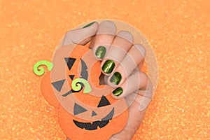 Female hand with green nail design. Glitter green nail polish manicure. Female hold orange paper halloween pumpkins on glitter