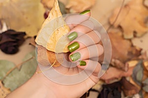 Female hand with green nail design. Woman hand hold dry leaves. Green autumn nail polish manicure with golden glitter