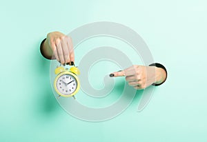 Female hand hold alarm clock and point to it through a hole on neon mint background. Minimalistic creative isolated just