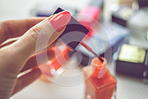 Female hand hold brush with red nail polish. A table with a bunch of nail polishes of different colors in blur