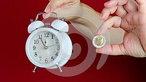 Female hand hold coin 2 euro and alarm clock on red background, concept of time, deadline, payments, savings