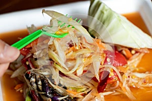 Female hand hold fork with Papaya salad, Thai food name Som Tum, on white plate