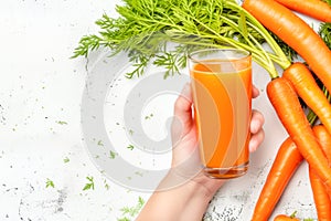 Female hand hold glass with fresh carrot juice against white background with natural young carrots