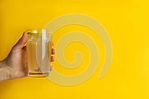 Female hand hold glass of ginger beer on yellow background