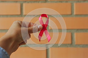 Female hand hold pink awareness ribbon on brick wall background