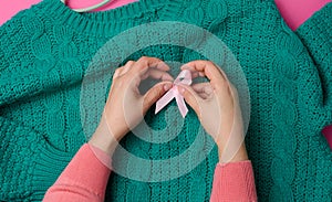 Female hand hold a pink silk ribbon in the form of a loop on a pink background. Symbol of the fight against breast cancer