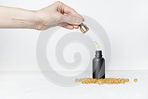 Female hand hold pipette and drop oil to black Cosmetic bottle where near cod-liver oil on white background