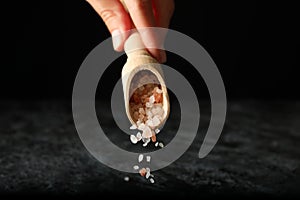 Female hand hold scoop with pink himalayan salt on black background