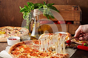 Female hand hold slice of hot pizza with melting cheese and chorizo on rustic wooden table with ingredients