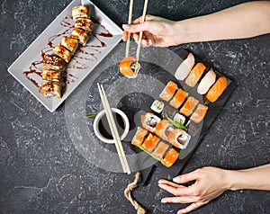 Female hand hold sushi roll with chopsticks on black stone background