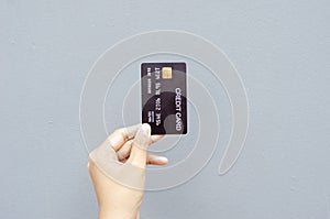 female hand holding a black credit card mockup with security chip embedded on a gray background