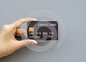 female hand holding a black credit card mockup with security chip embedded on a gray background