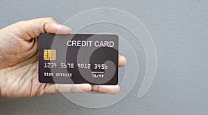 female hand holding a black credit card mockup with security chip embedded on a gray background with copy space