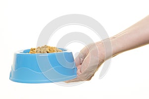 Female hand holding blue plastic feeding bowl filled with cat kibble isolated on a white background